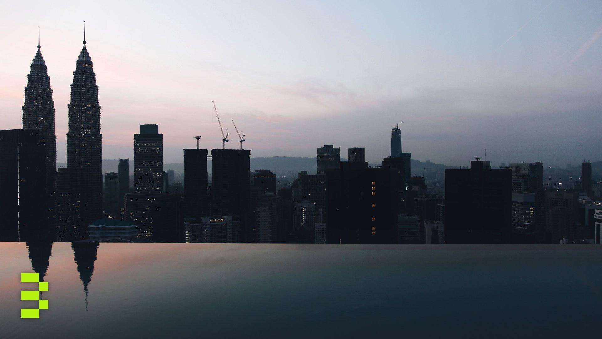 Twilight view of the Kuala Lumpur skyline and the Petronas Twin Towers reflected in an infinity pool.