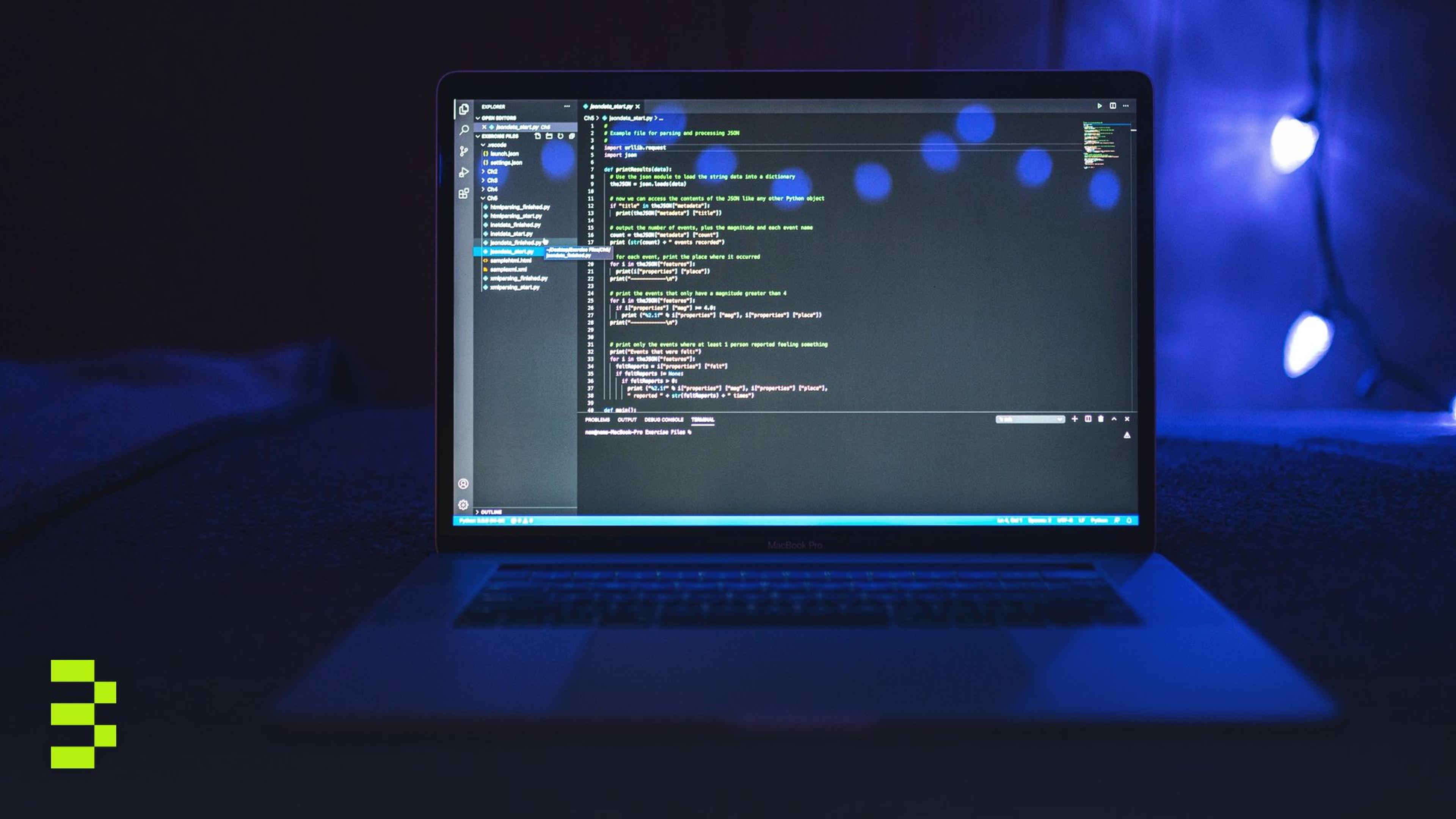 A laptop on a dark desk showing a code editor full of Python, lit by blue light from behind