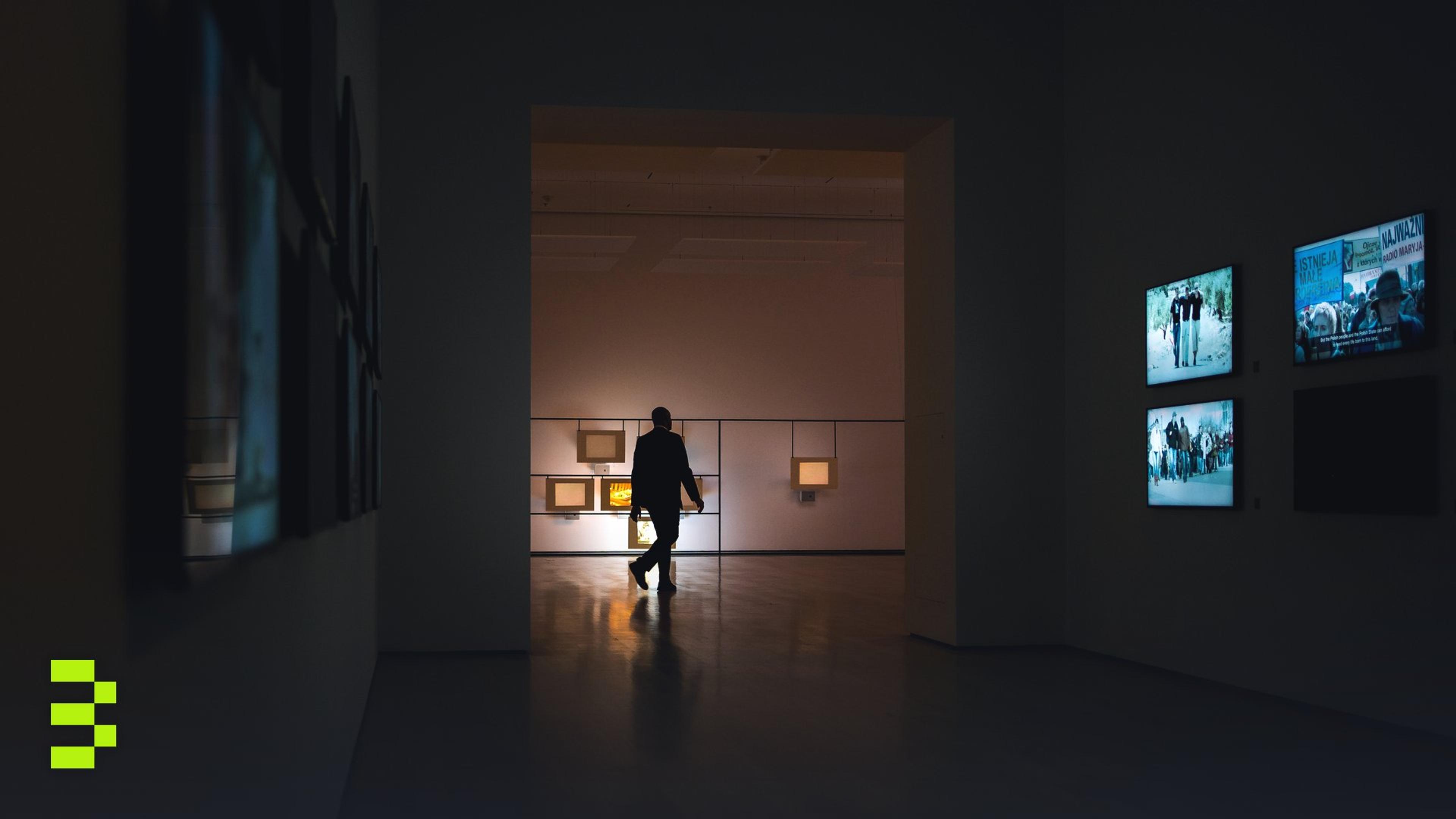 Silhouette of a man walking through a dimly lit art gallery surrounded by illuminated screens.
