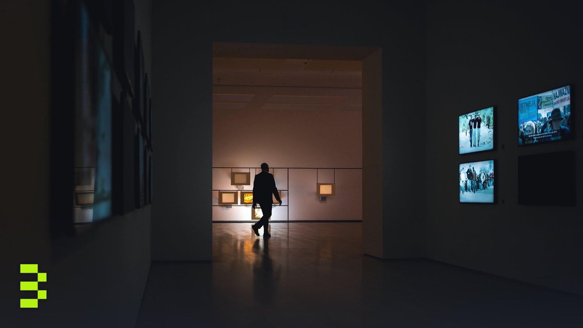Silhouette of a man walking through a dimly lit art gallery surrounded by illuminated screens.