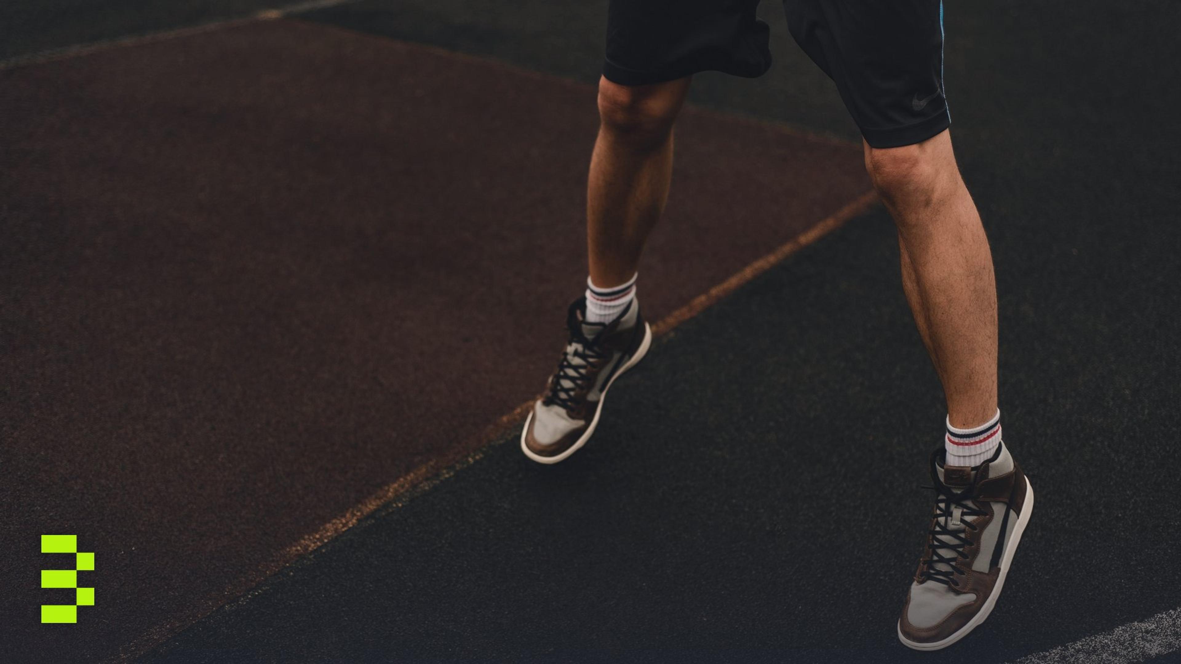 Close-up of an athlete's legs and sneakers on an outdoor basketball court.