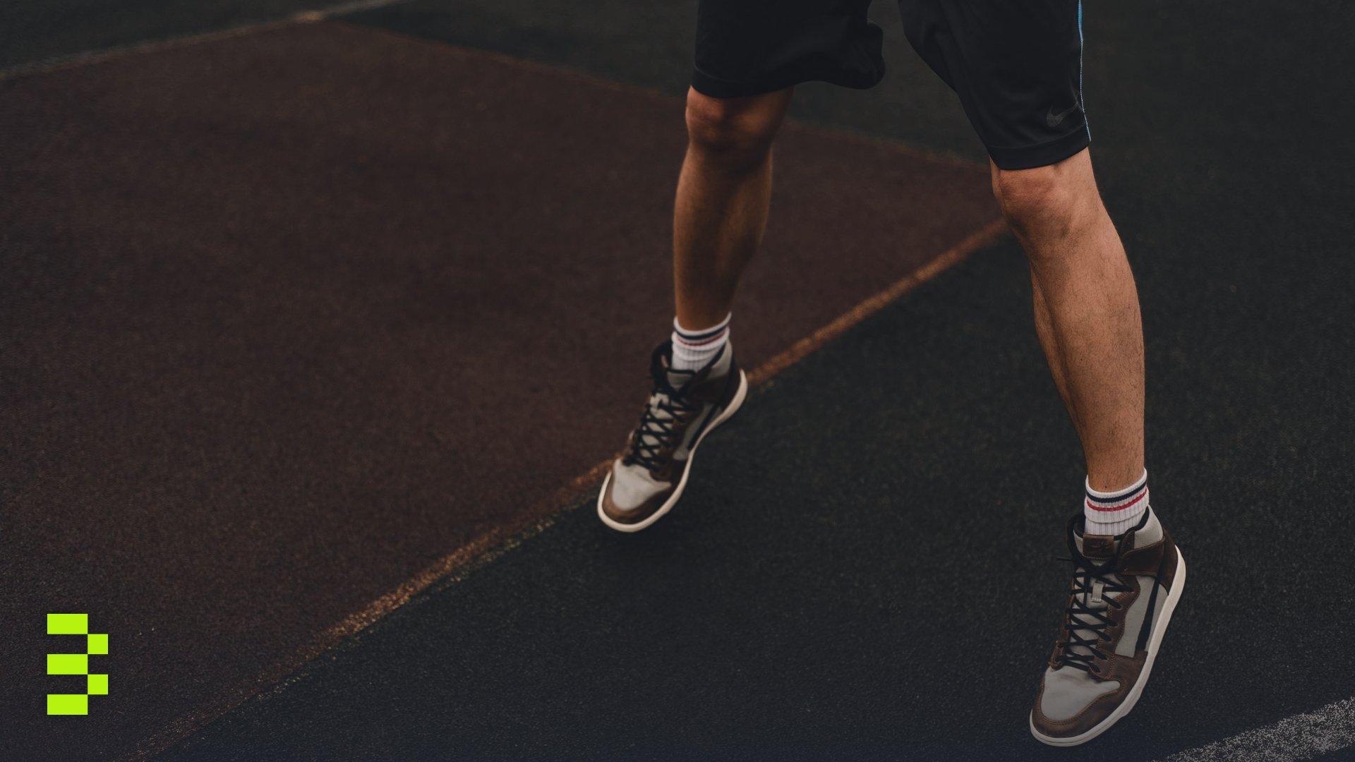 Close-up of an athlete's legs and sneakers on an outdoor basketball court.