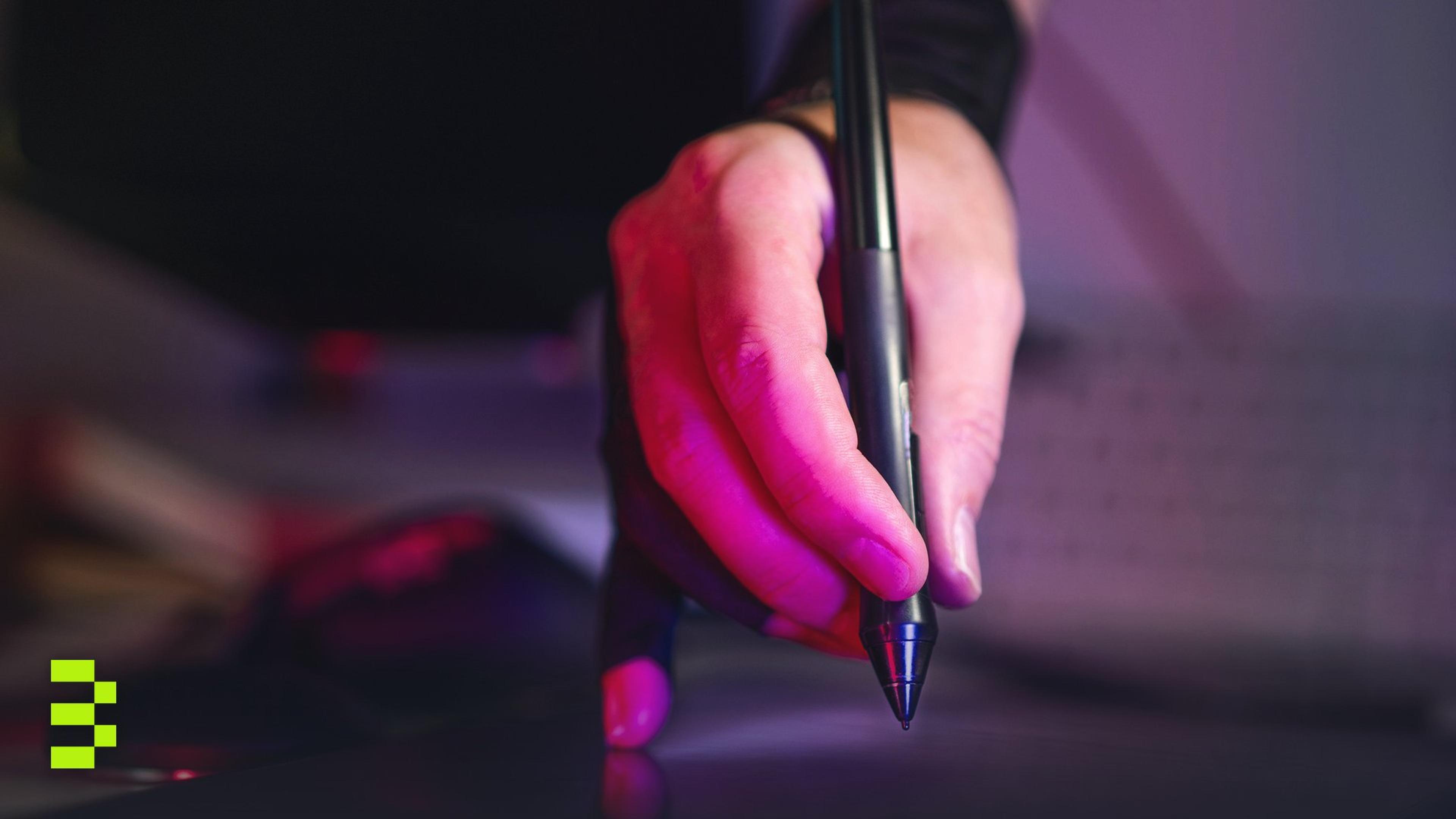 A digital artist's hand working on a graphics tablet with a stylus, in a creative studio setting.