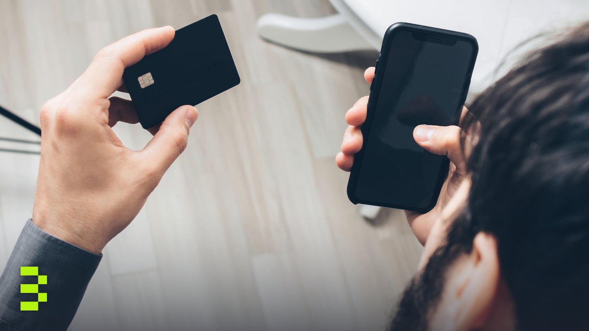 Close-up of a man holding a smartphone and a credit card while making an online payment.