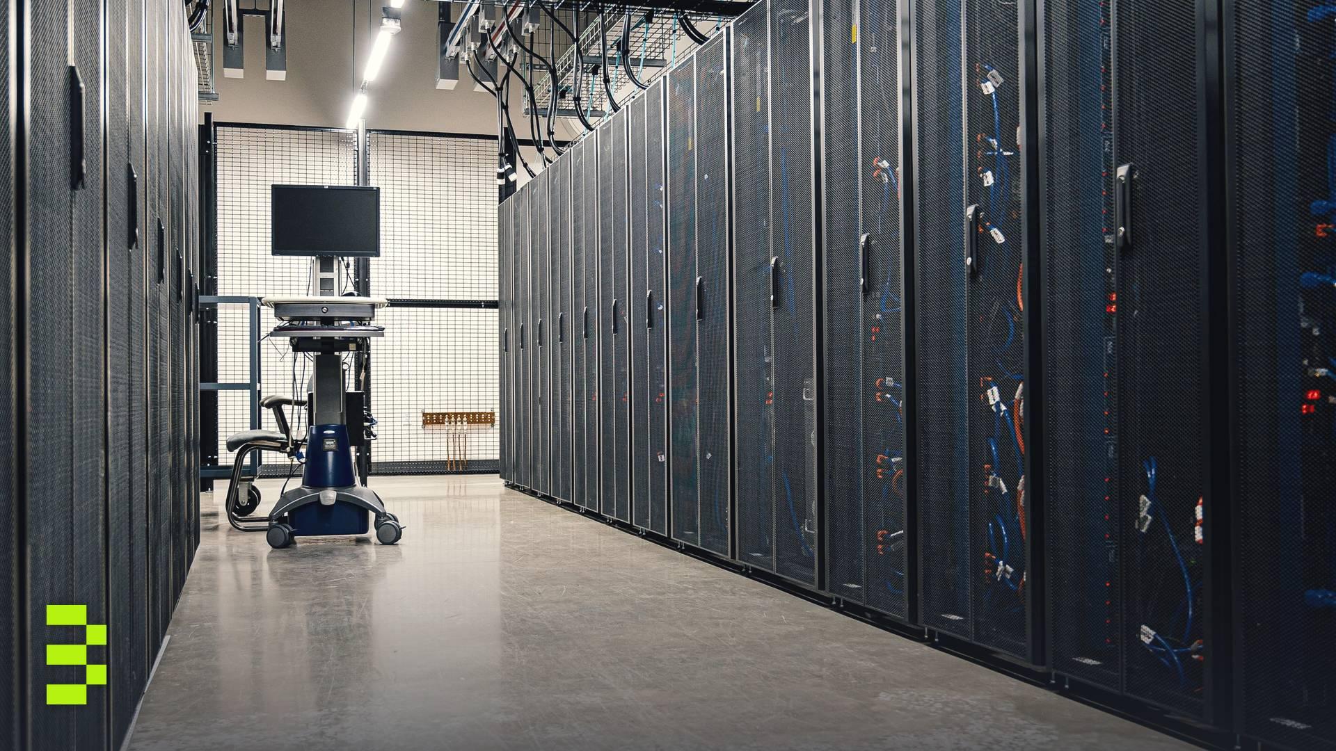 A long aisle of black server racks with blue and orange cabling in a brightly lit data center, with a monitor cart at the far end