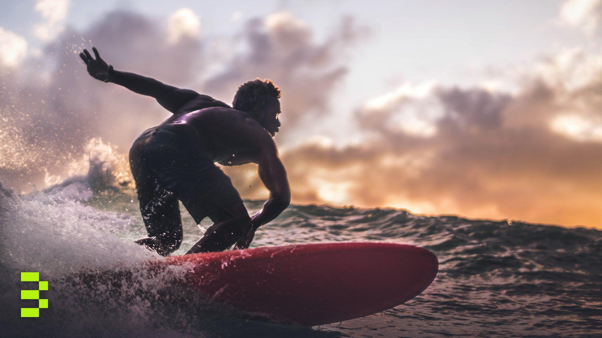 A surfer rides the waves during a vibrant sunset.