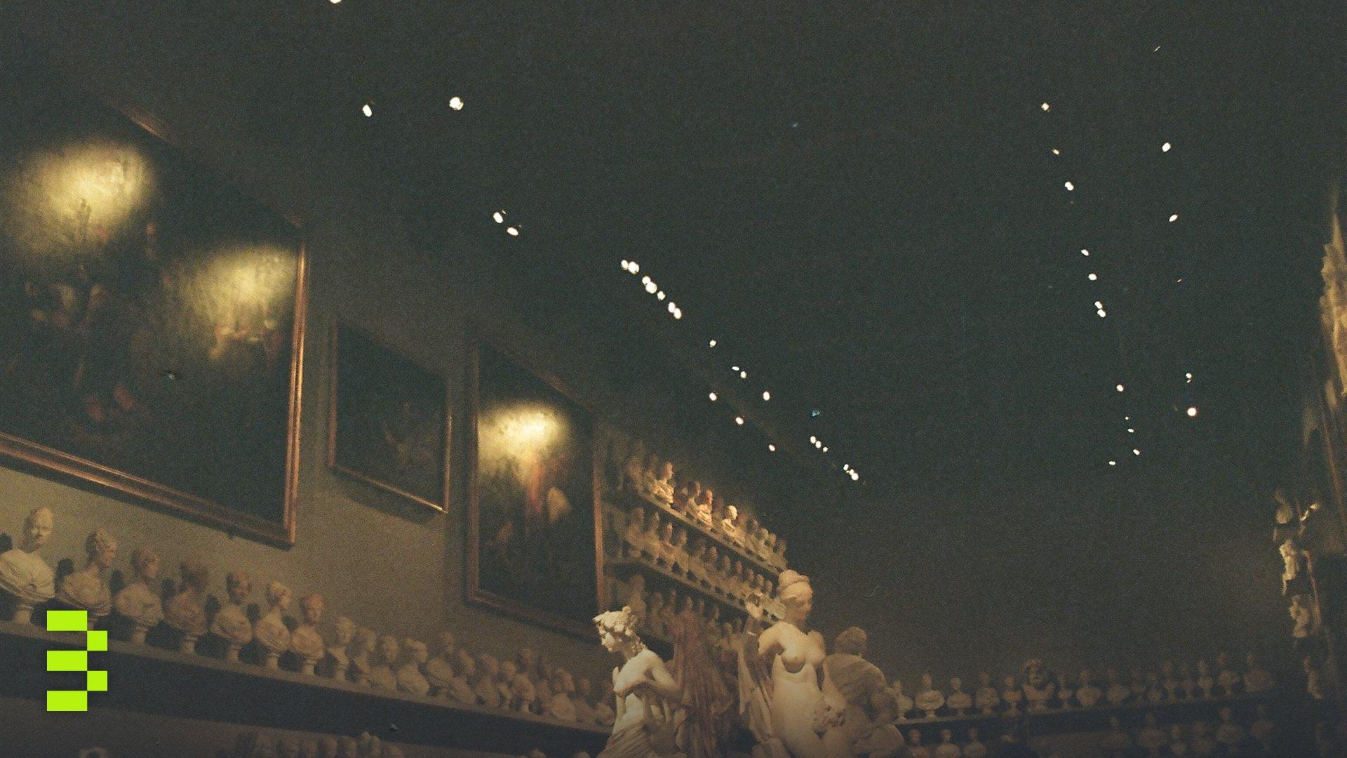 Dimly lit museum gallery with sculptures, busts, and classical paintings.