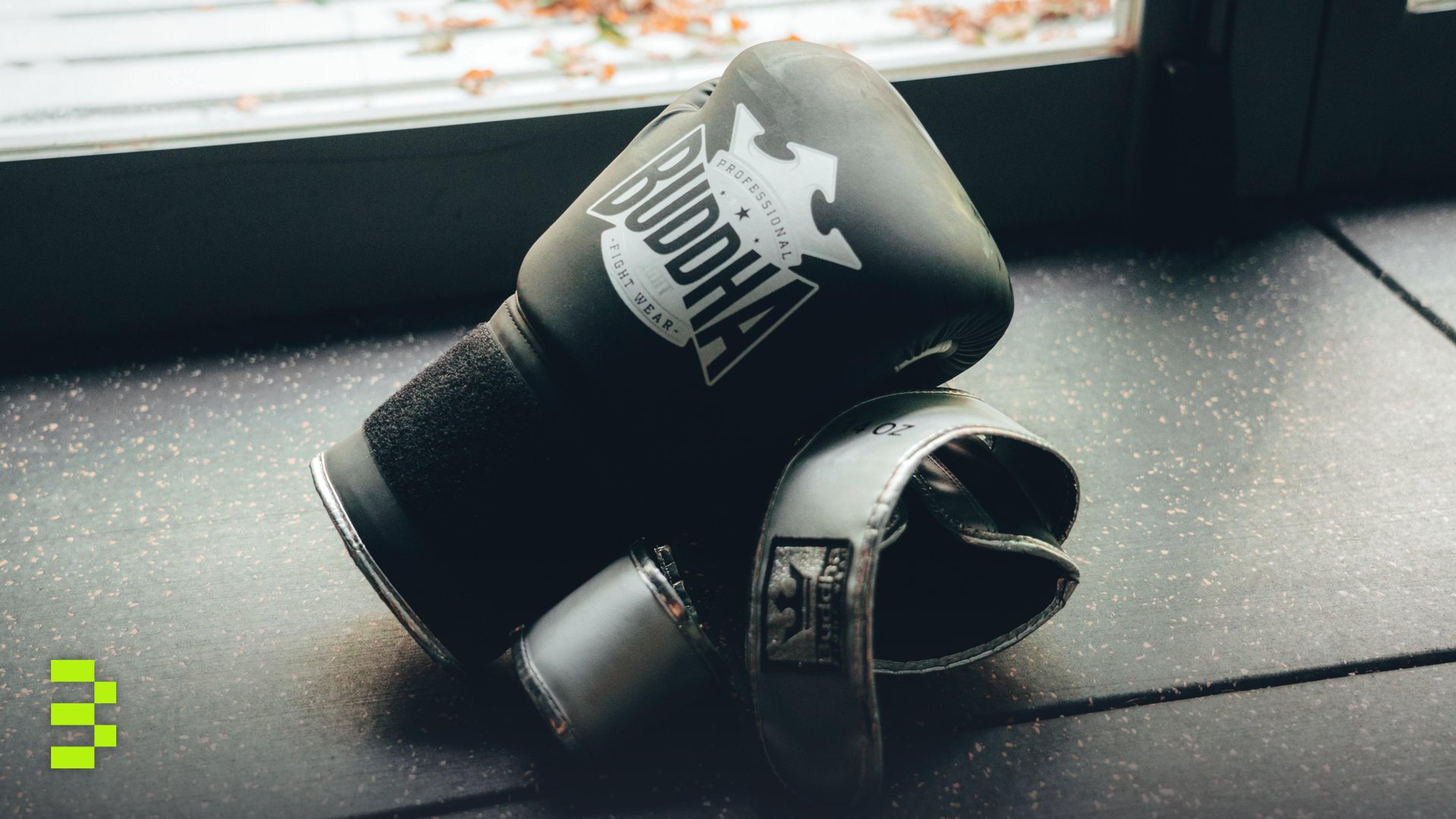 A pair of black boxing gloves lying on a gym floor near a window.
