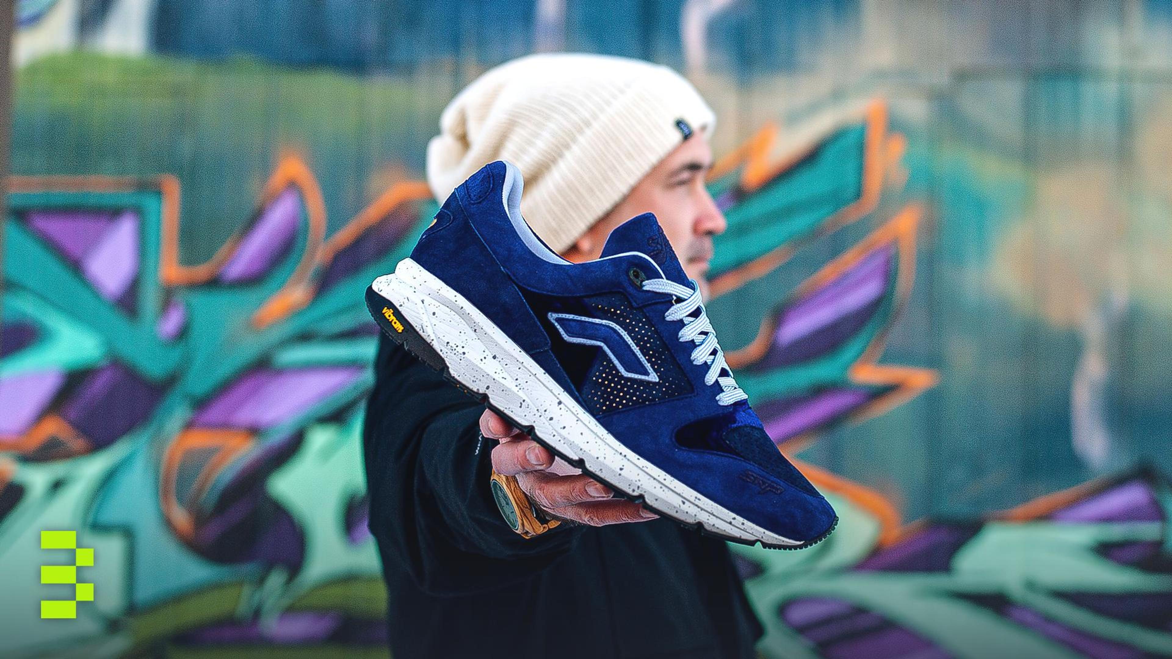 Stylish man presenting blue sneaker against vibrant urban graffiti.