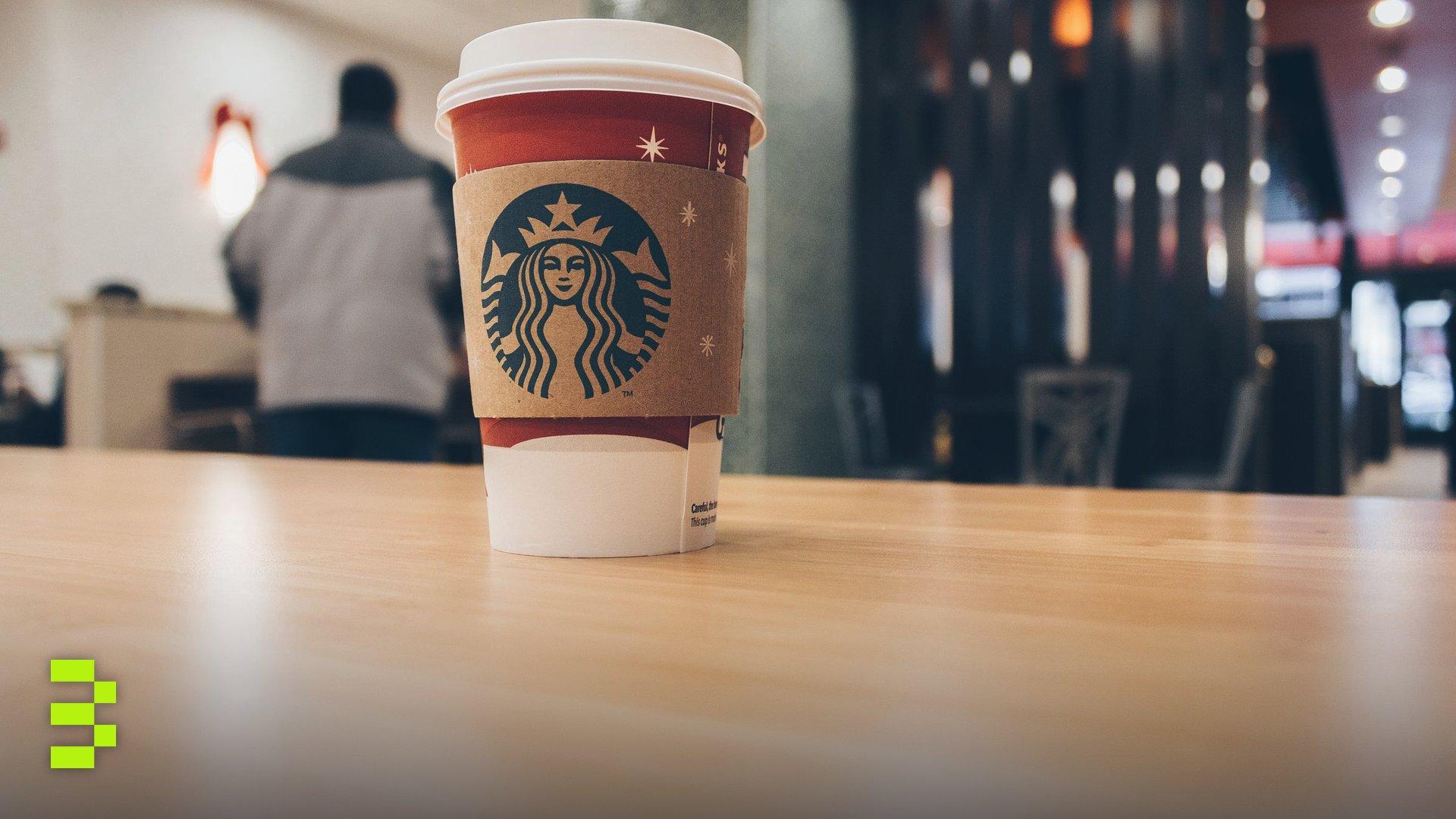 Close-up of a Starbucks coffee cup on a wooden table in a cozy café setting.