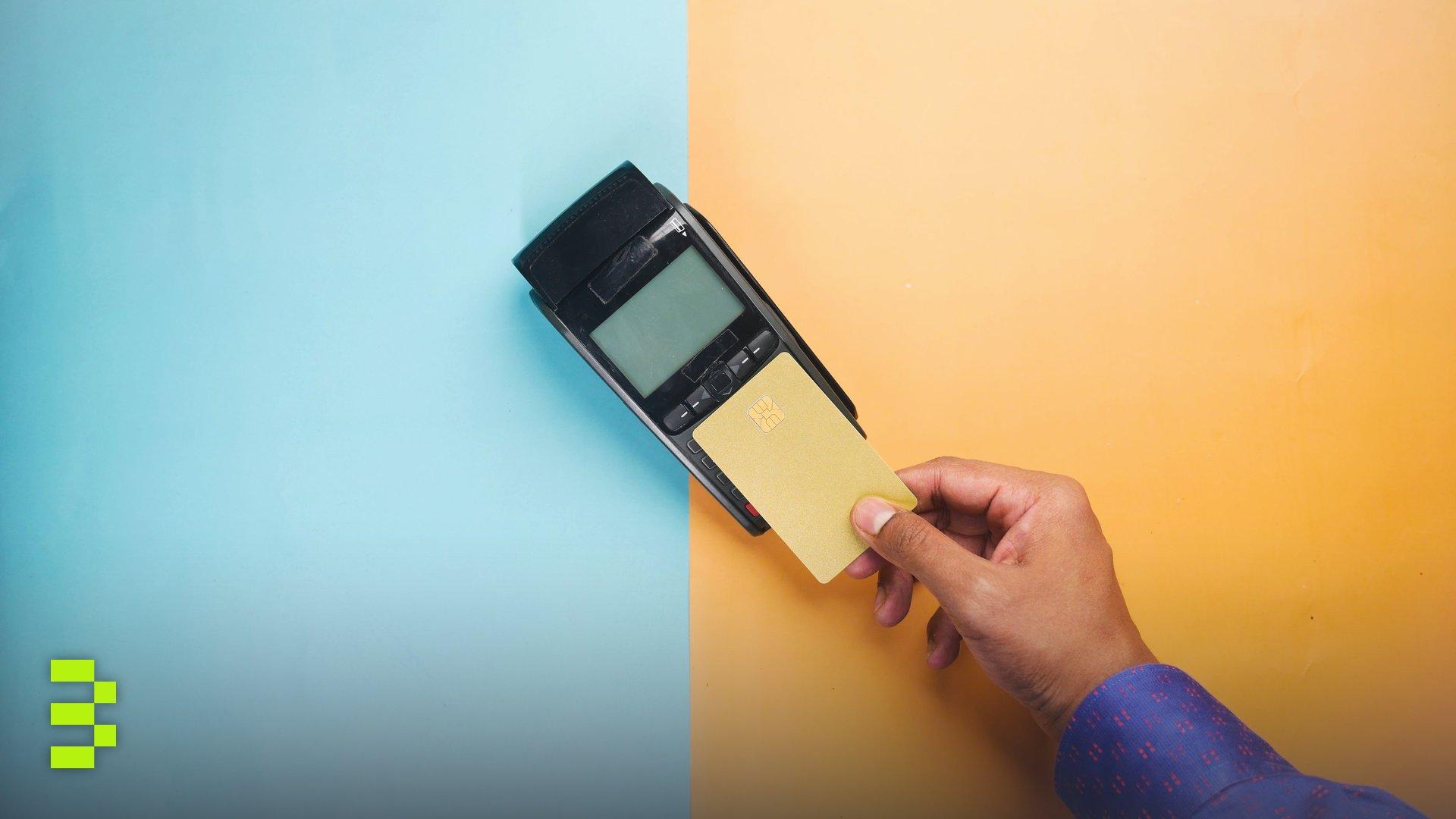 A hand tapping a credit card on a payment terminal for a contactless transaction.