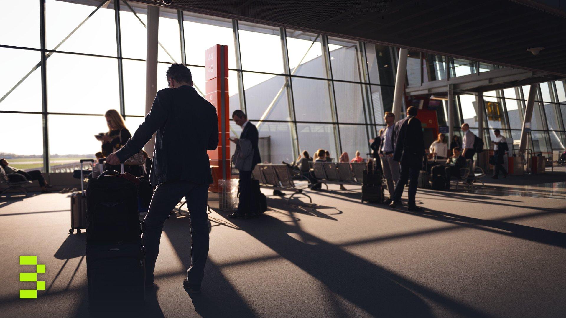 Travelers in a bustling airport terminal with carry-on luggage waiting for departure.