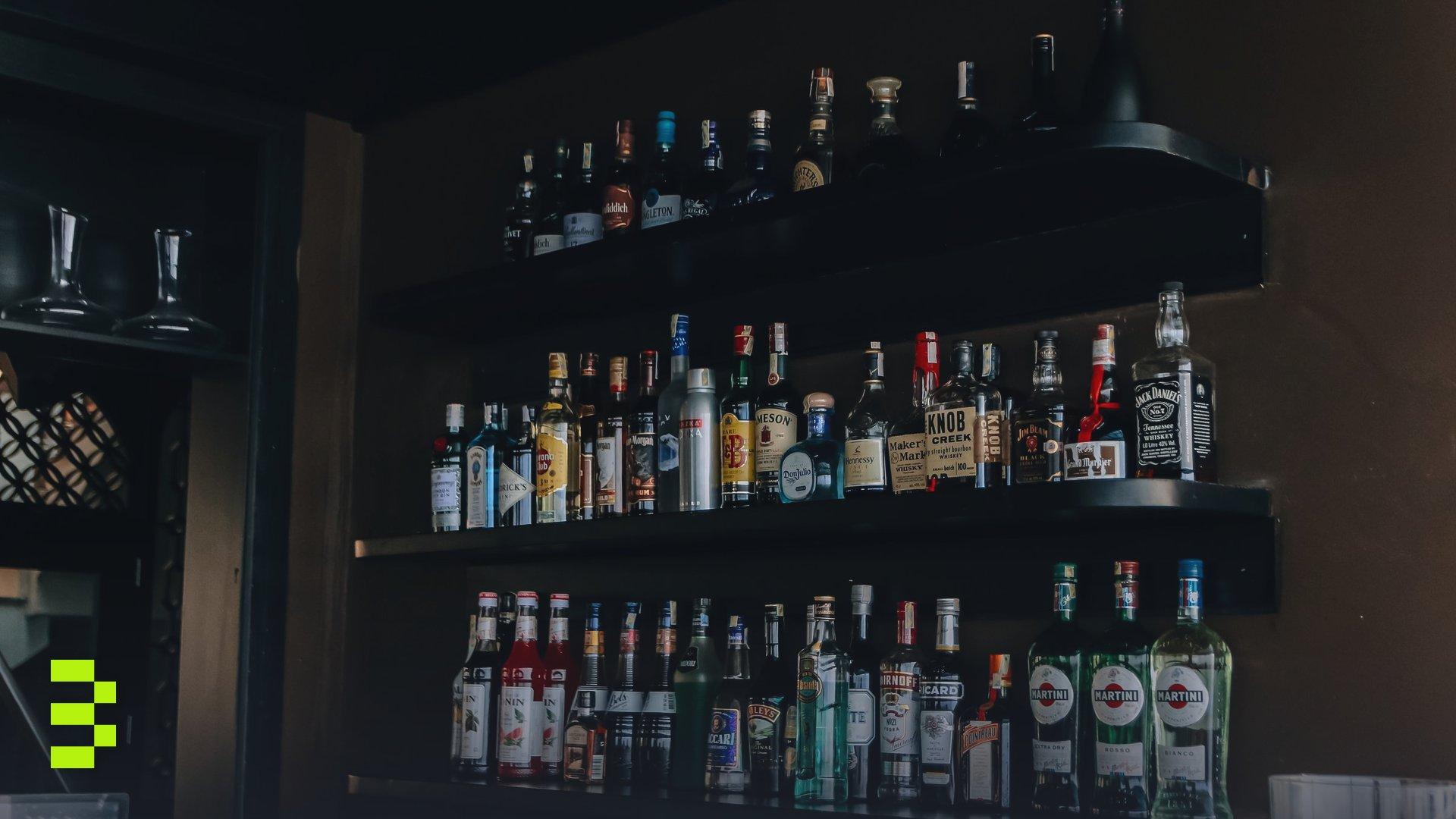A modern bar with a wide selection of liquor bottles arranged on sleek black shelves.