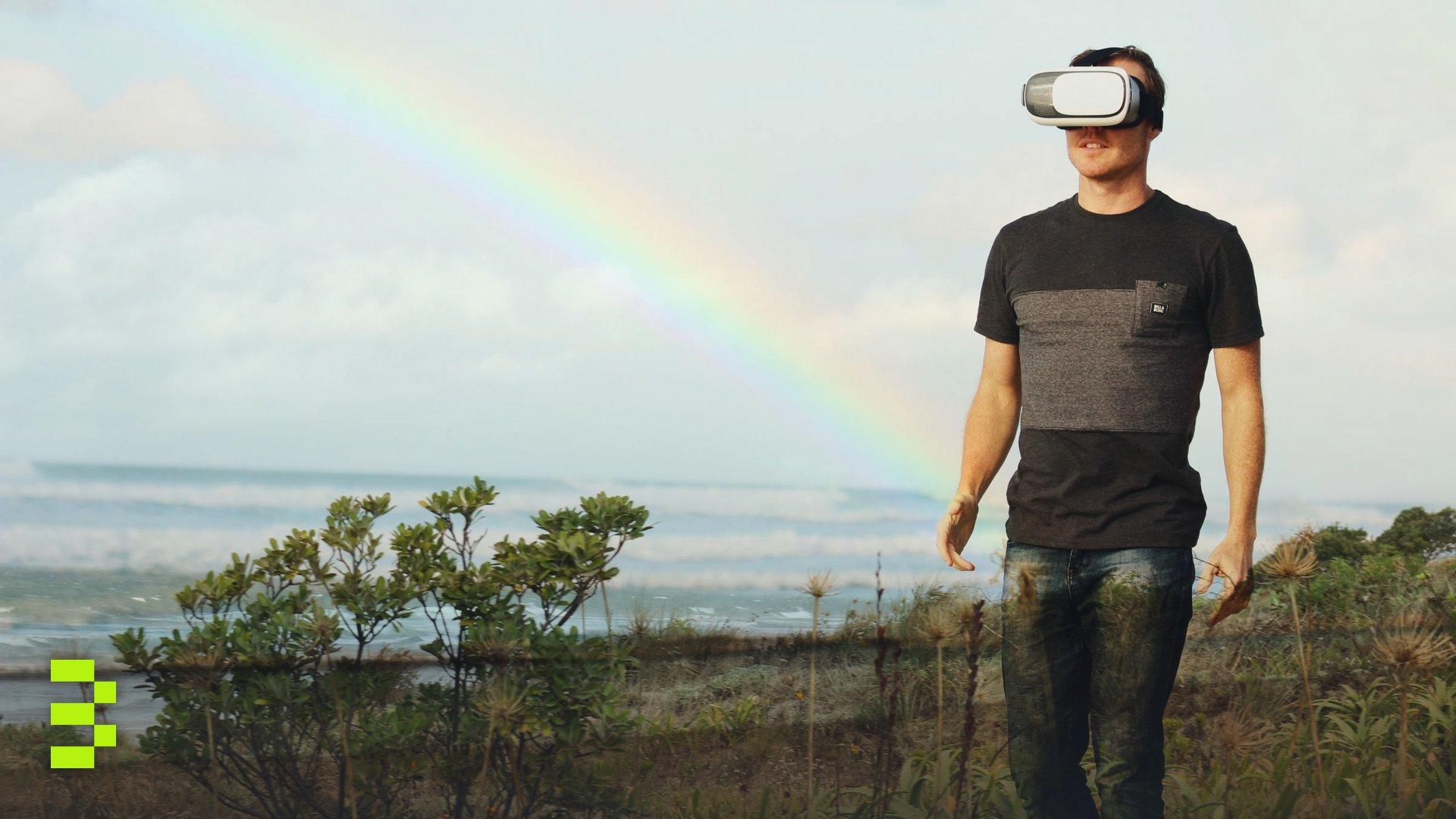 Man using VR headset walks in nature under a rainbow.