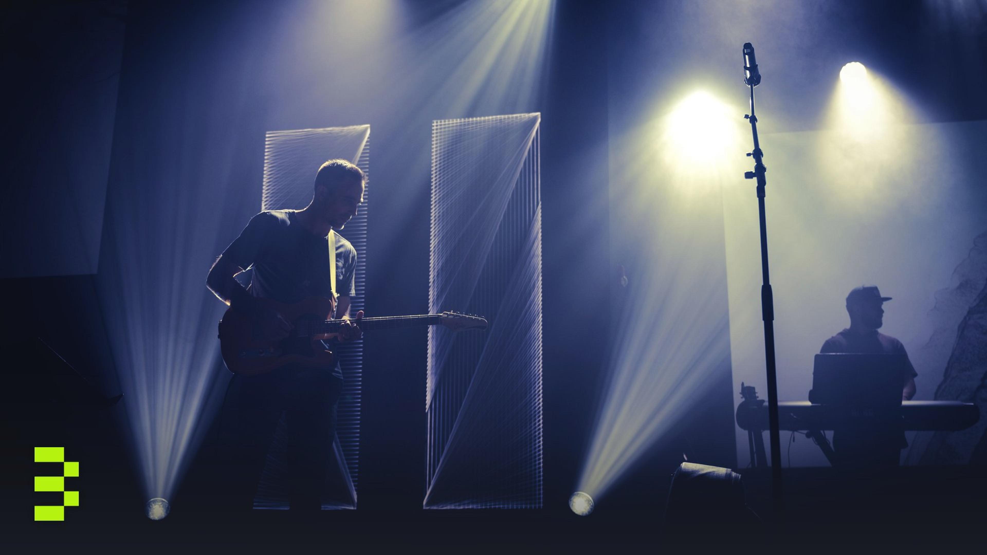 In a dimly lit club, a guitarist and keyboardist perform live on stage.