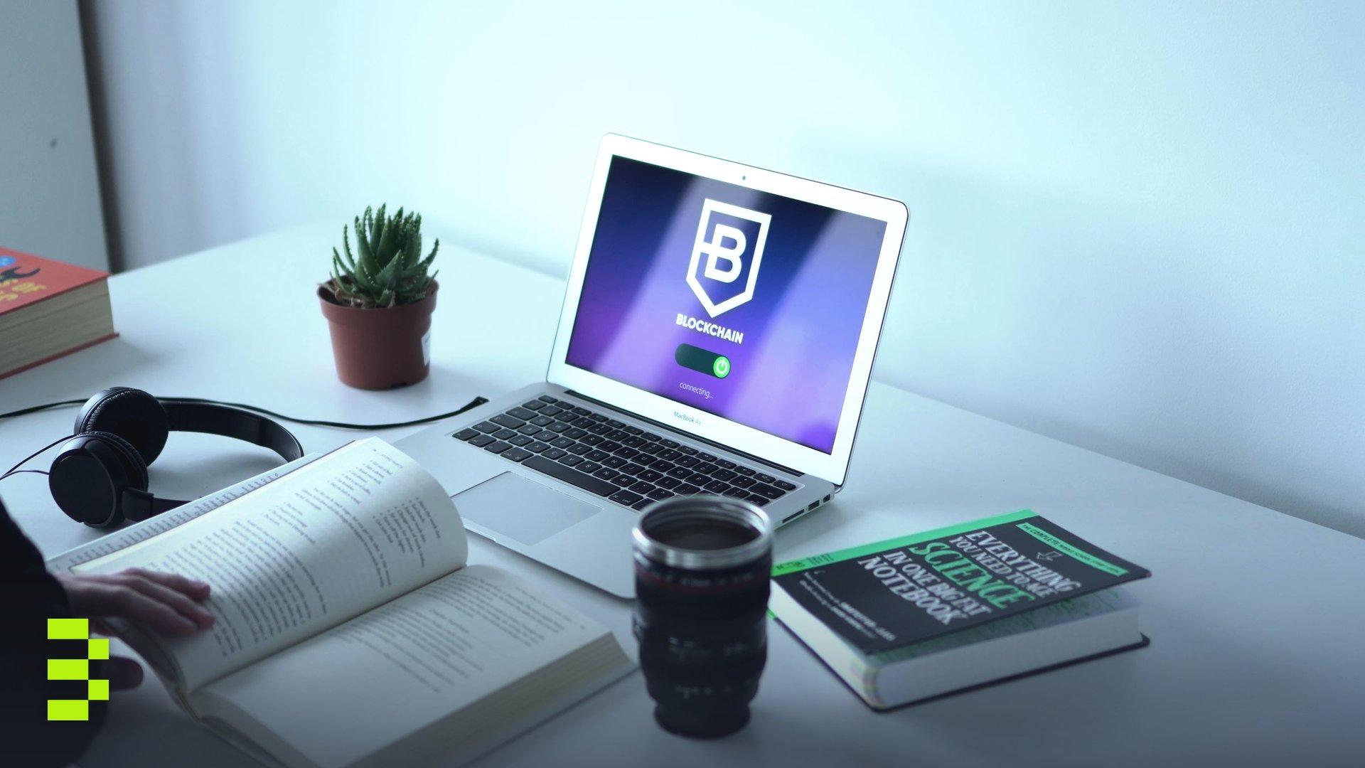 A laptop displaying blockchain technology in a modern workspace with books and headphones.