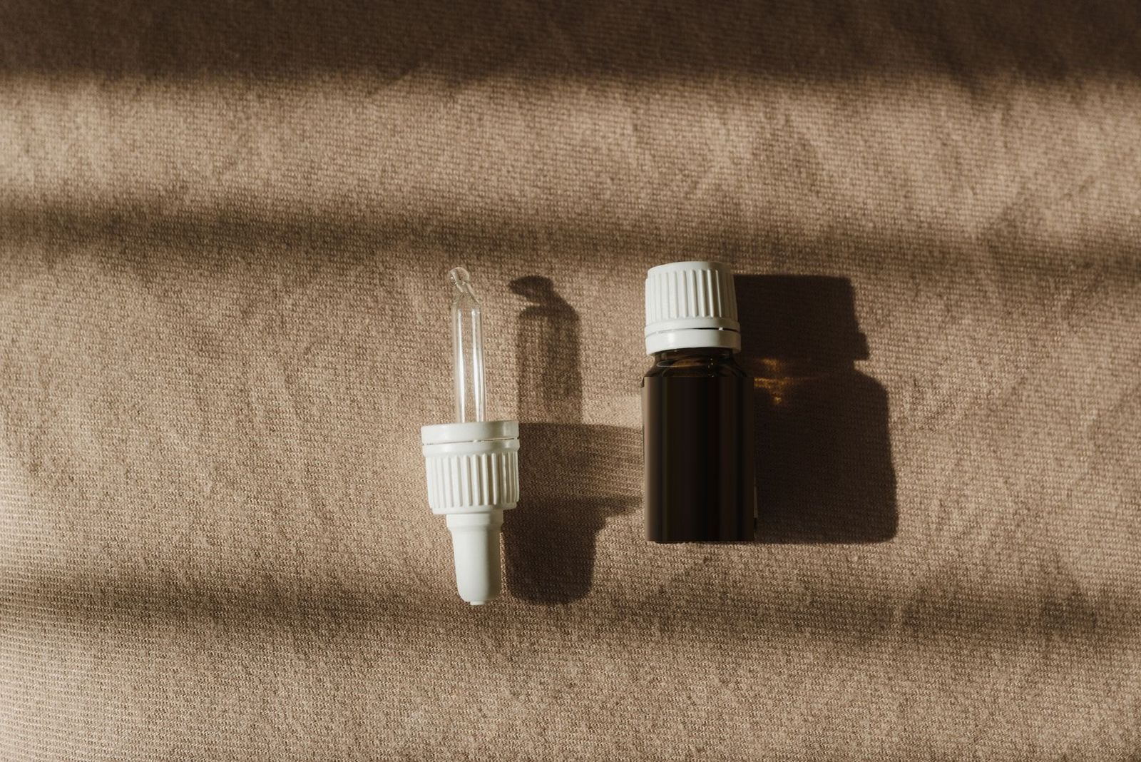 A dropper and an amber bottle on brown textile