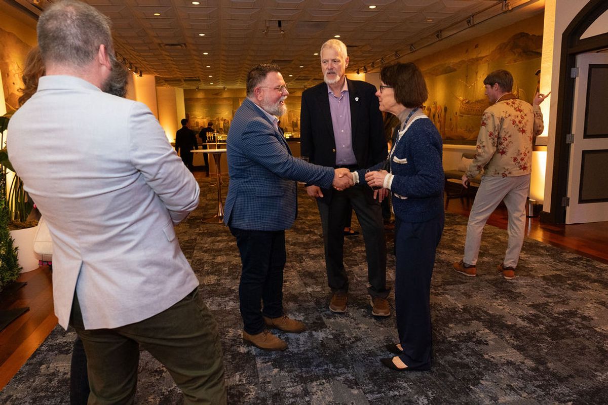 Business professionals networking and shaking hands in an upscale venue with warm lighting and carpeted.