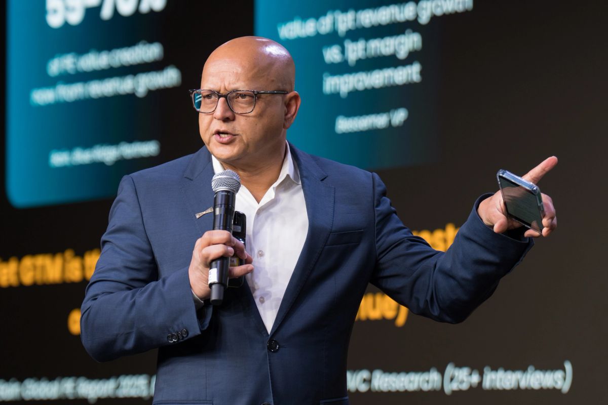 Bald speaker in dark suit presenting with microphone and mobile device at business conference