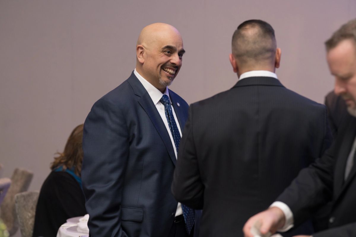 Smiling bald man in dark suit interacting with other formally dressed attendees at an indoor event