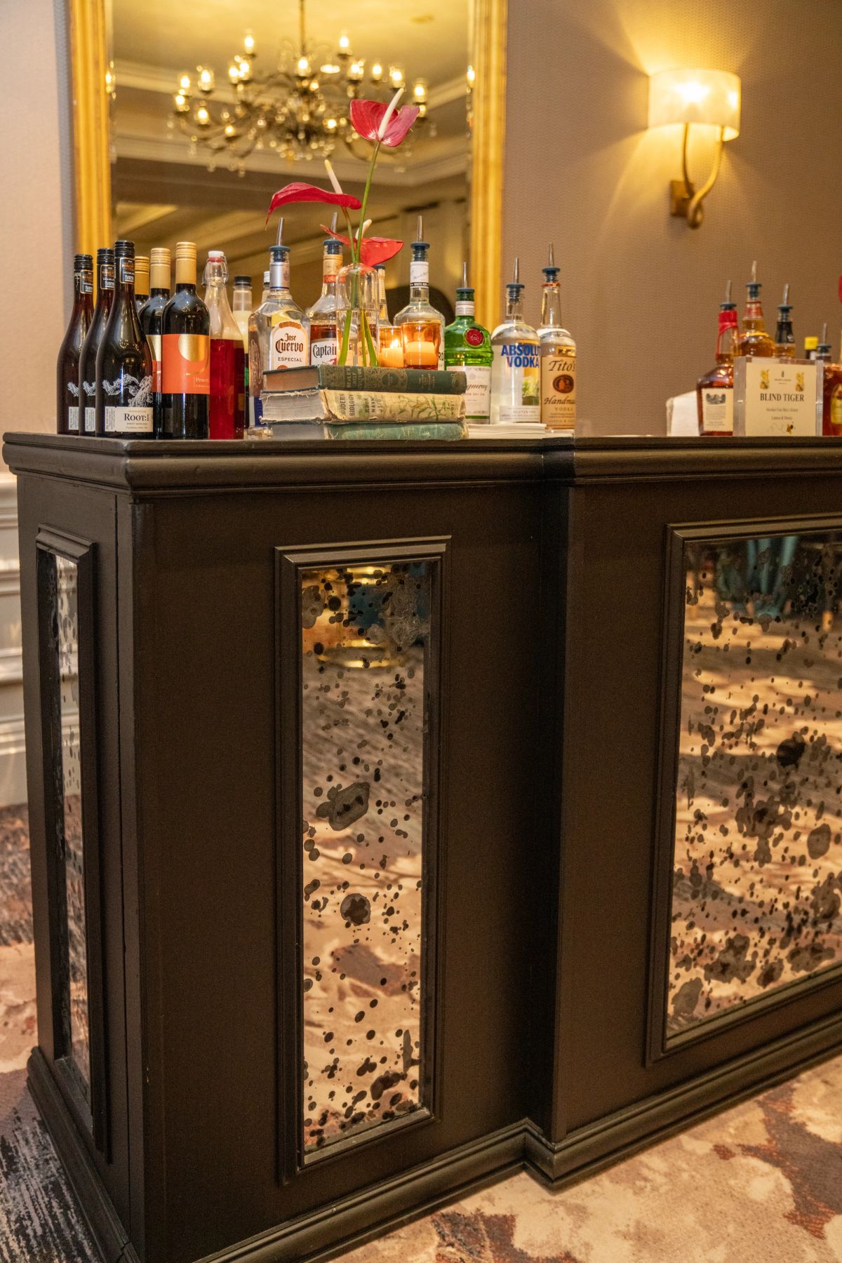 Elegant home bar with dark wood cabinetry, mirrored panels, various liquor bottles, and decorative flowers