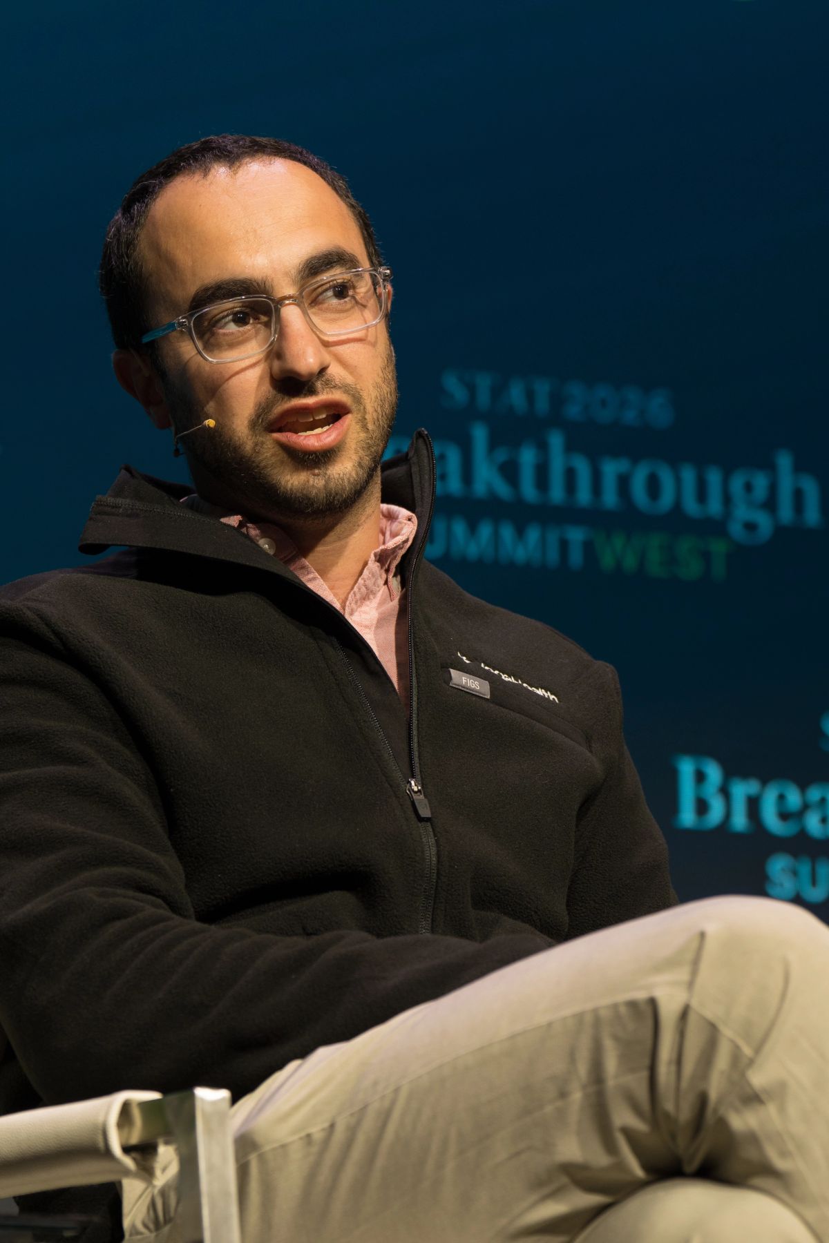 Speaker in black jacket and glasses sits during panel discussion at Commonwealth Club event