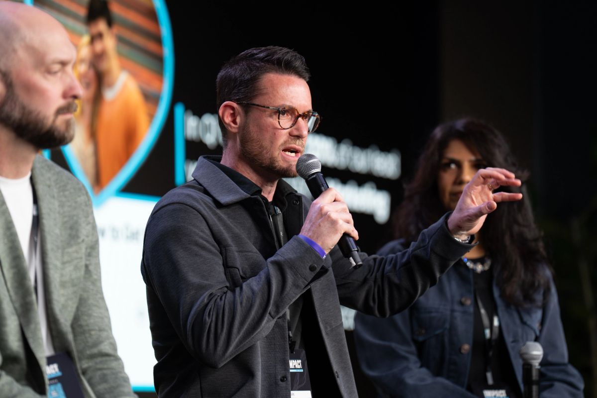 Speaker with microphone gesturing while presenting at conference panel with other attendees seated nearby