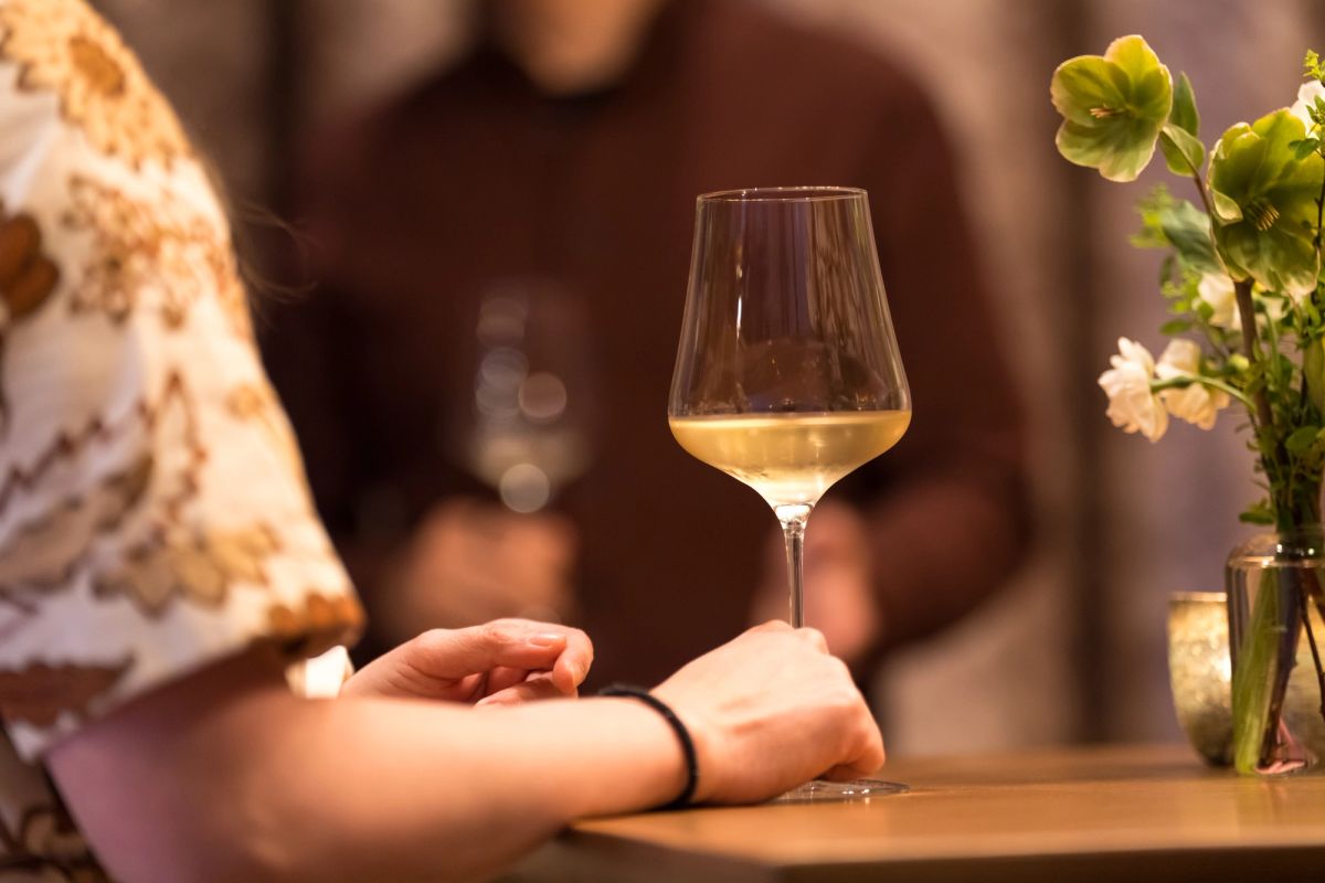 Person holds wine glass at table with flowers during indoor event