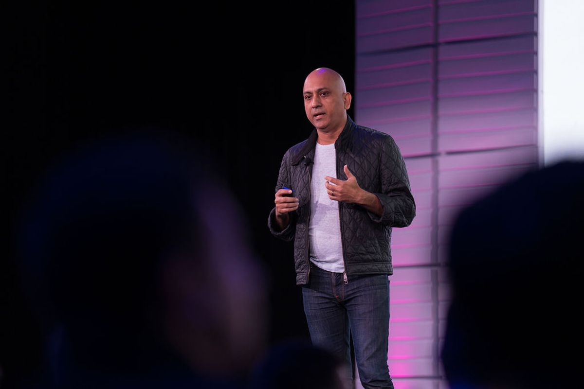 Speaker presenting on stage with purple lighting and geometric backdrop