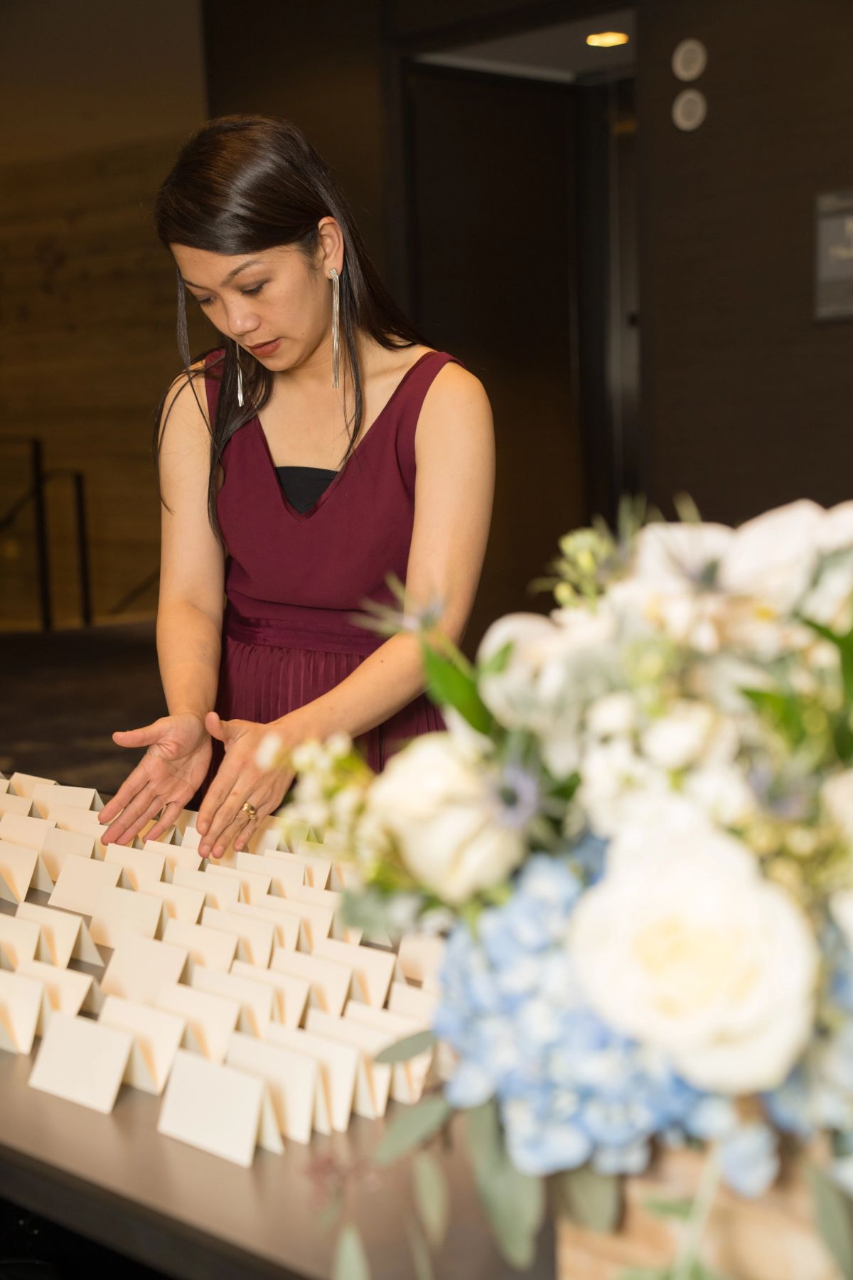 Woman in burgundy dress arranging white place cards on table next to white and blue floral arrangements