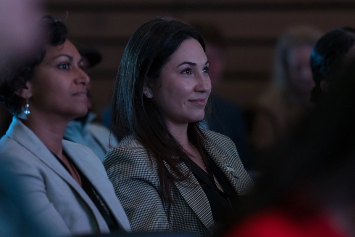 Two women in business attire sitting and smiling while attending a conference presentation
