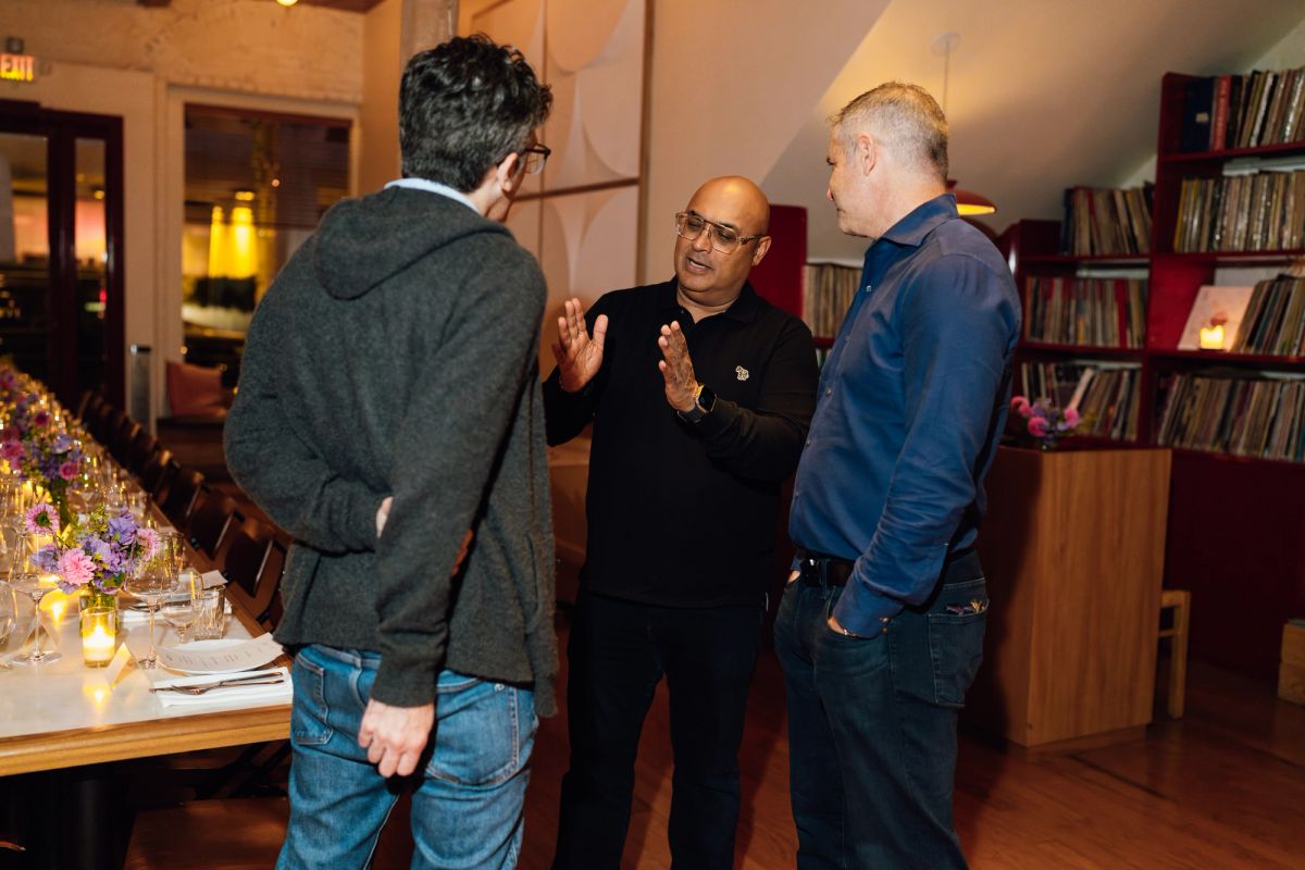 Three men in business casual attire networking and conversing in a restaurant dining room with bookshelves.
