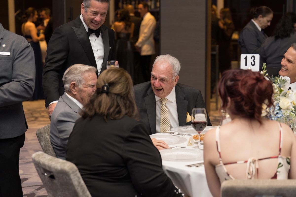 Formal dinner event with guests in evening wear seated at tables, servers attending to diners