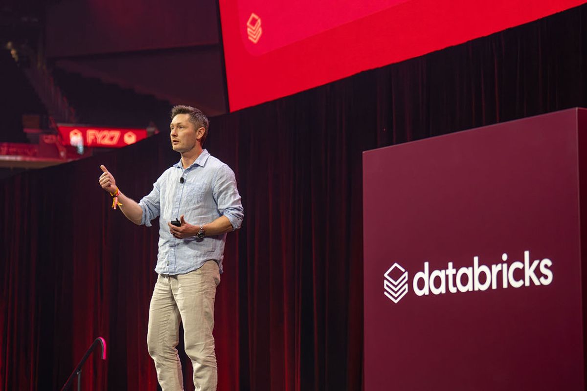 Speaker presenting on stage at Databricks conference with red and purple lighting and branded backdrop