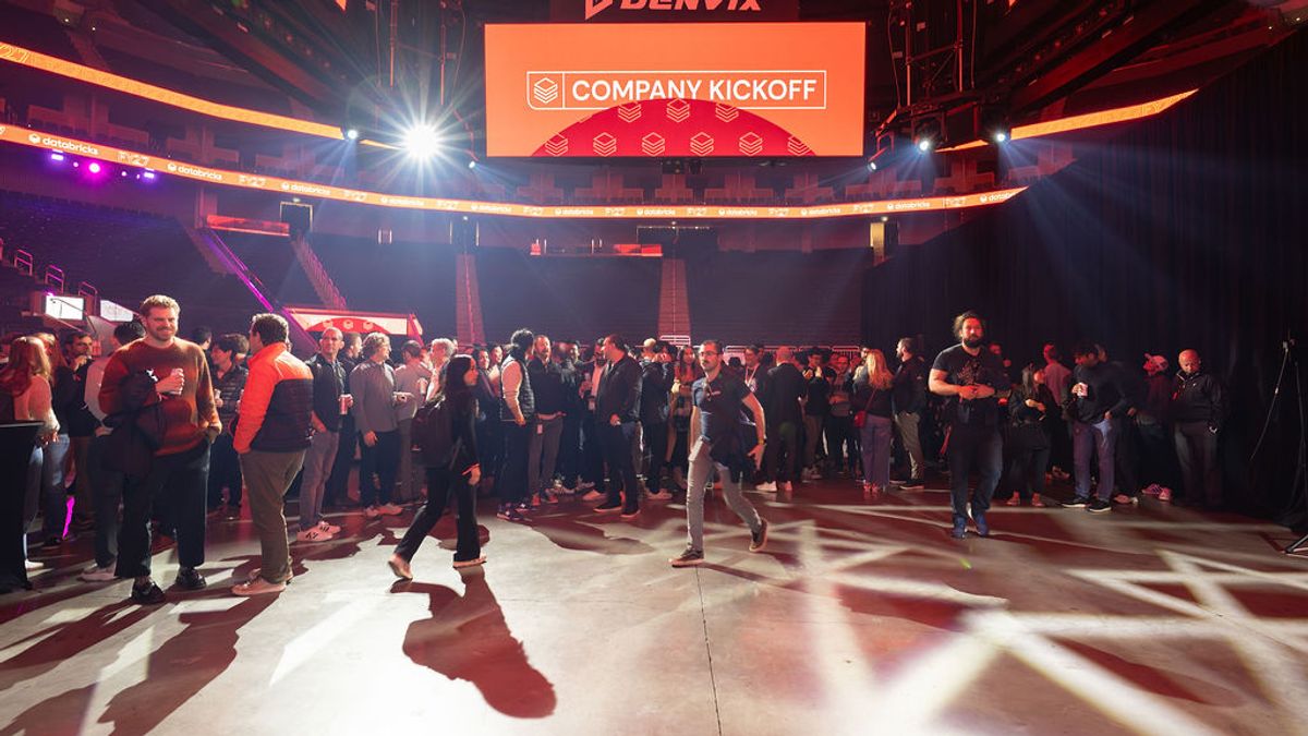 Corporate event attendees networking in arena venue with Company Kickoff banner and colorful stage lighting