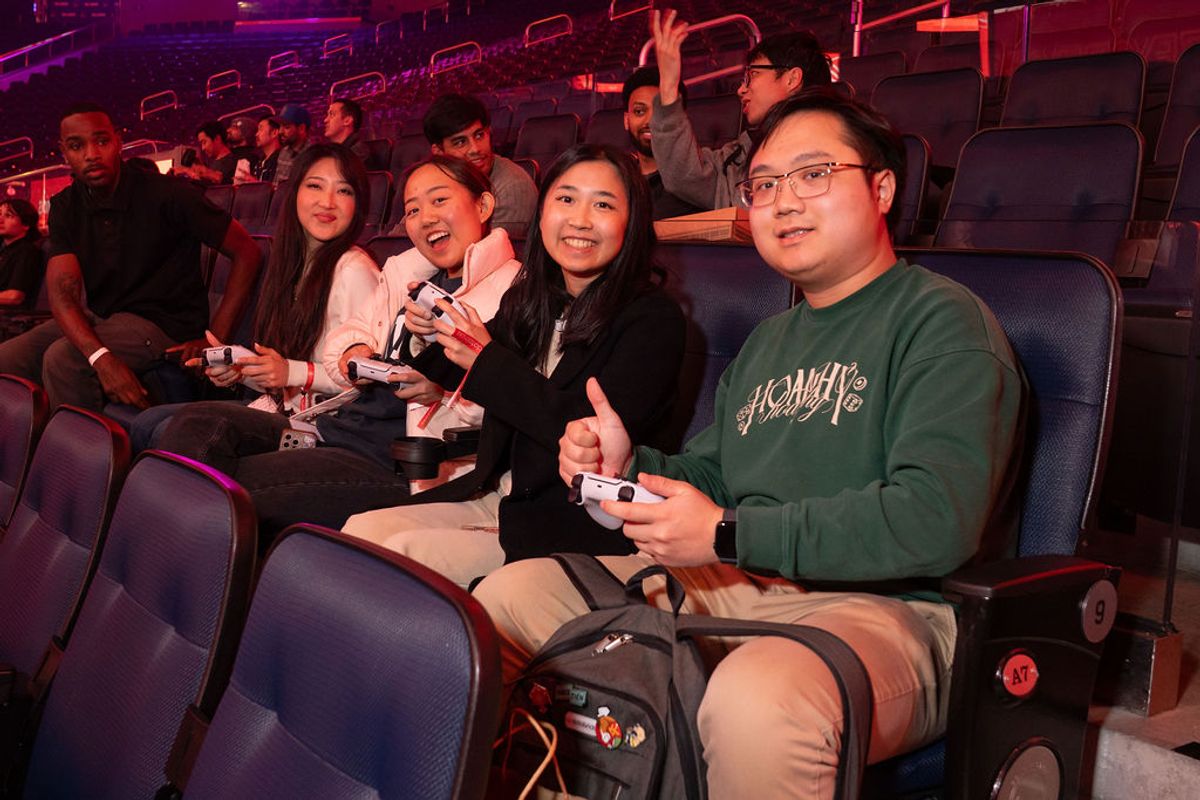 Four attendees smile and hold gaming controllers while seated in purple venue chairs with colorful lighting
