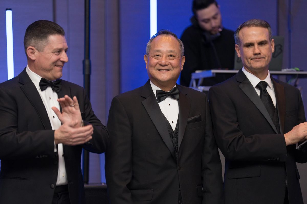Three men in formal black suits and bow ties standing together at an elegant evening event