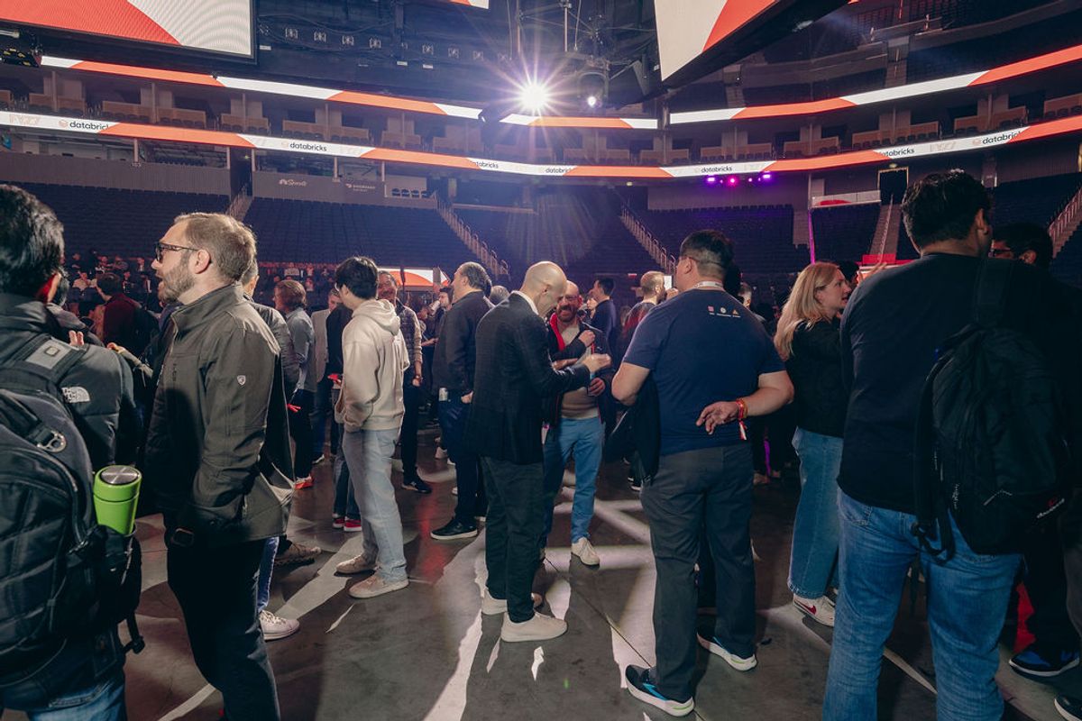 Conference attendees networking in arena venue with tiered seating and stage lighting visible overhead