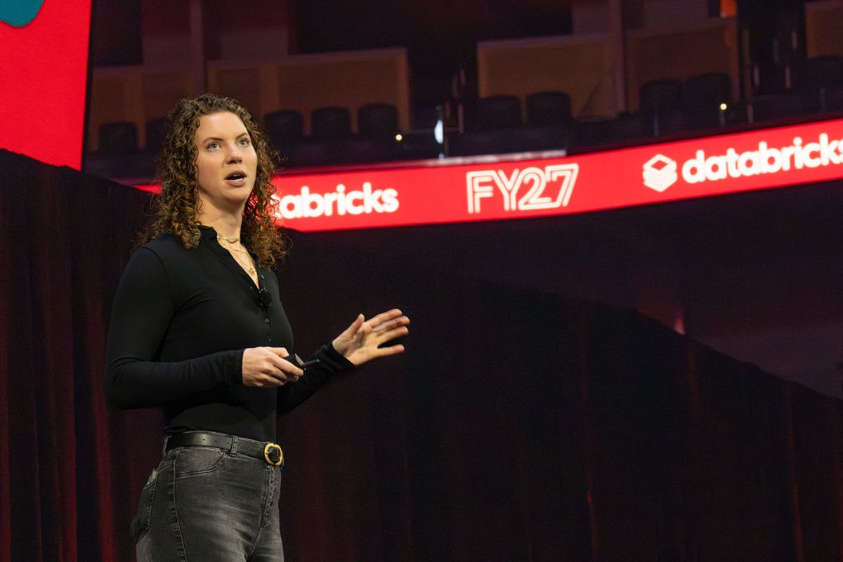 Speaker presenting on stage at conference with Databricks FY27 branding visible on backdrop