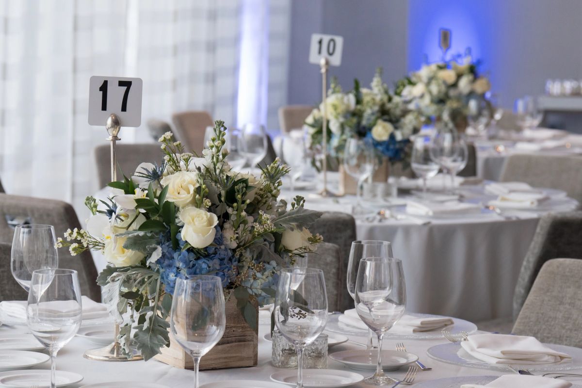 Elegant dinner tables with white floral centerpieces, table numbers 17 and 10, wine glasses, and blue.