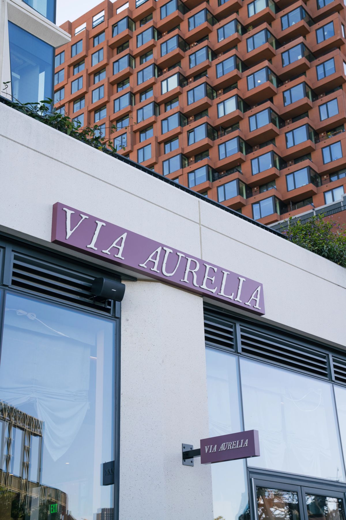 Via Aurelia building entrance with purple signage and red brick residential tower in background