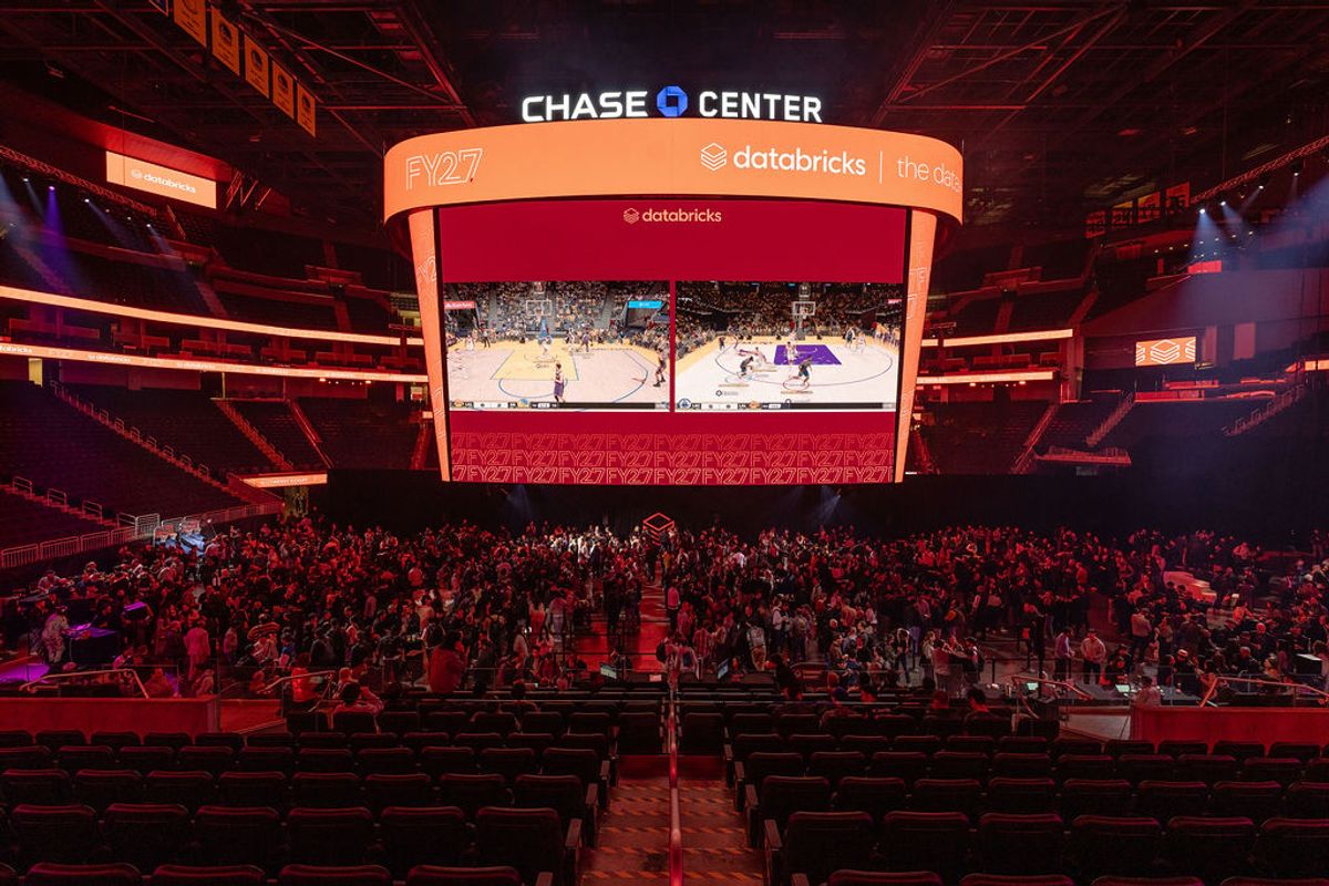 Conference attendees at Chase Center arena with large screen displaying databricks event content