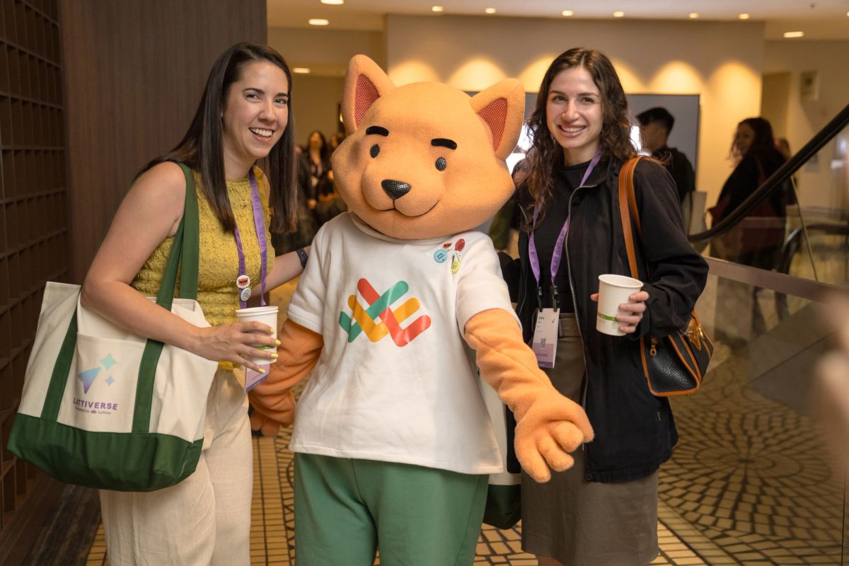 Two attendees pose with a fox mascot holding coffee cups at a conference.
