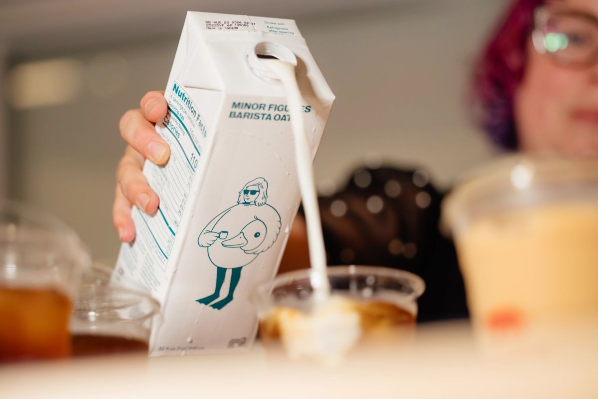 Hand holding white milk carton with cartoon character design at coffee shop counter with drinks