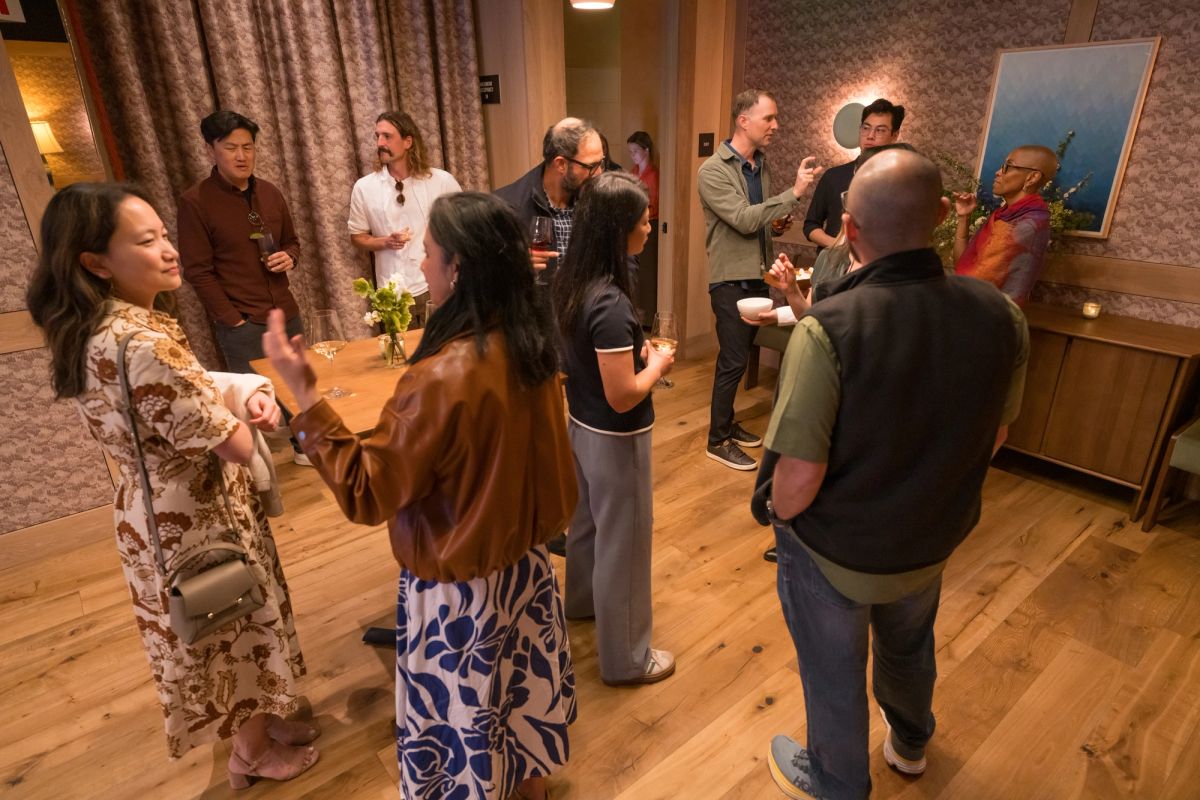 Group of people socializing and networking in a warmly lit room with wooden floors and patterned wallpaper.