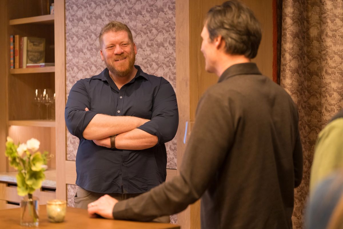 Two men having a conversation in a modern kitchen setting, one with arms crossed smiling at the other