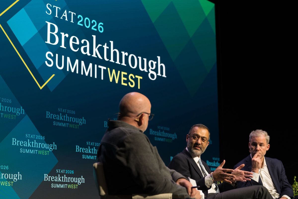 Three men in business attire sit on stage in discussion at STAT 2026 Breakthrough Summit West conference.