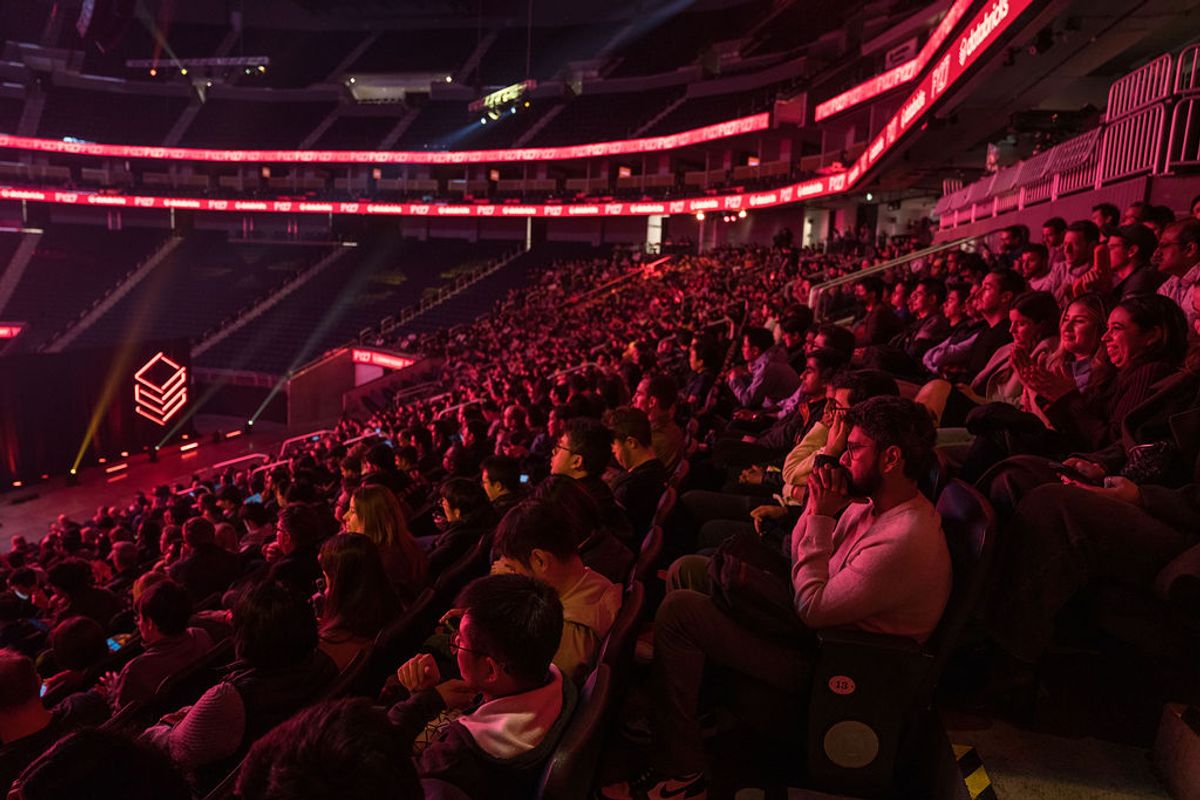 Large crowd of conference attendees seated in arena-style venue with red lighting and tiered seating