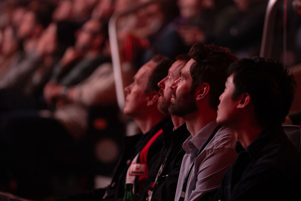 Conference attendees looking up and listening intently while seated in an auditorium with red lighting