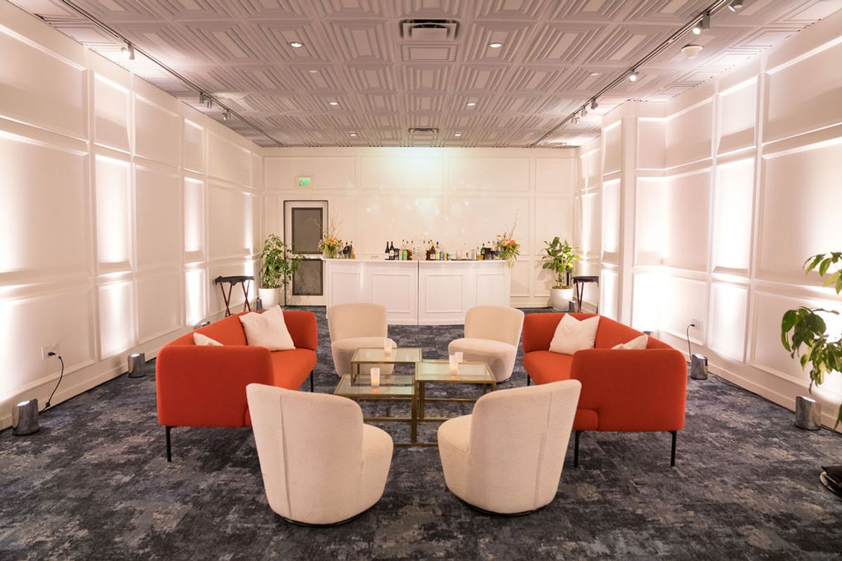 Modern lounge area with orange and beige chairs arranged around coffee table, white walls, track lighting.
